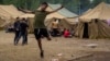 LITHUANIA -- A migrant jumps as other walk inside the newly built refugee camp in the Rudninkai military training ground, some 38km (23,6 miles) south from Vilnius, August 4, 2021